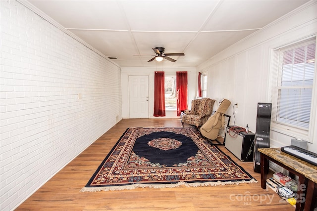 living area with hardwood / wood-style flooring, brick wall, and ceiling fan