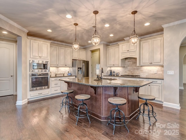 kitchen with decorative light fixtures, dark stone counters, a kitchen breakfast bar, stainless steel appliances, and a kitchen island with sink