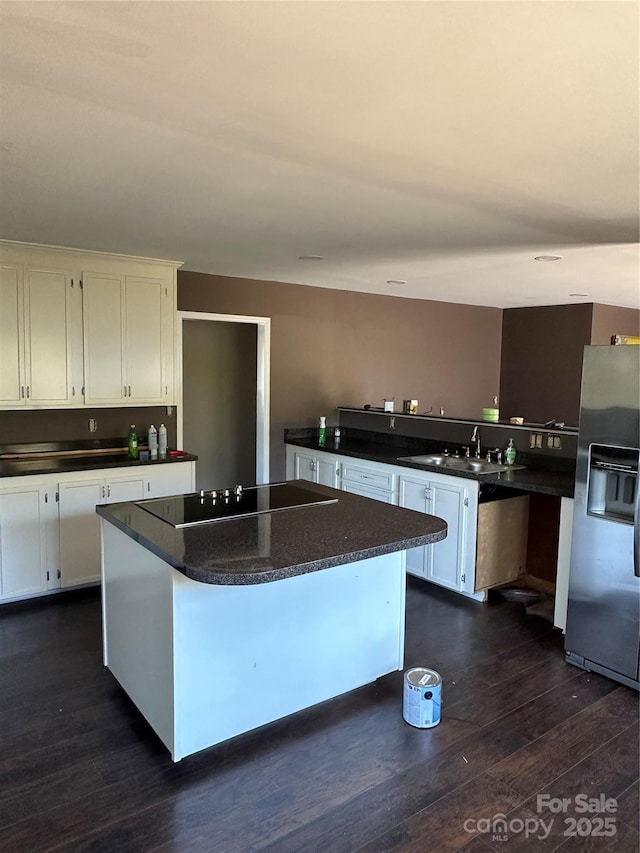 kitchen with white cabinets, black electric cooktop, stainless steel fridge, a kitchen island, and dark wood-type flooring