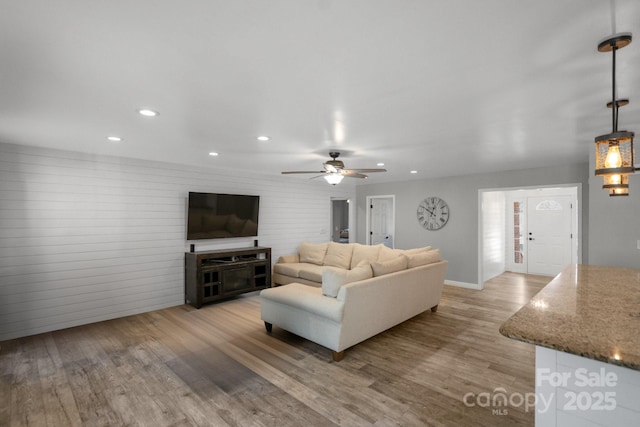 living room featuring ceiling fan, light hardwood / wood-style floors, and wooden walls