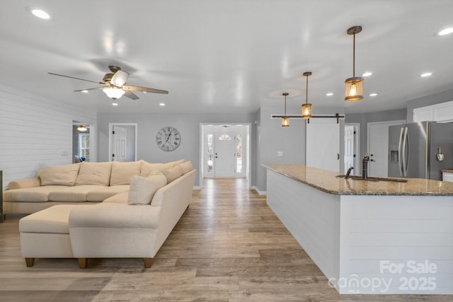 living room with light wood-type flooring, ceiling fan, a barn door, and sink