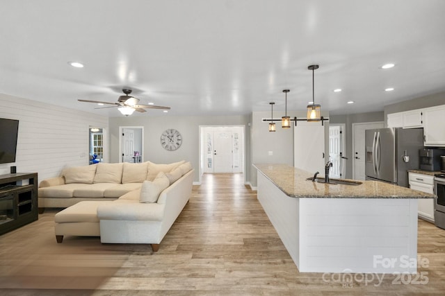 living room with ceiling fan, a barn door, sink, and light hardwood / wood-style flooring