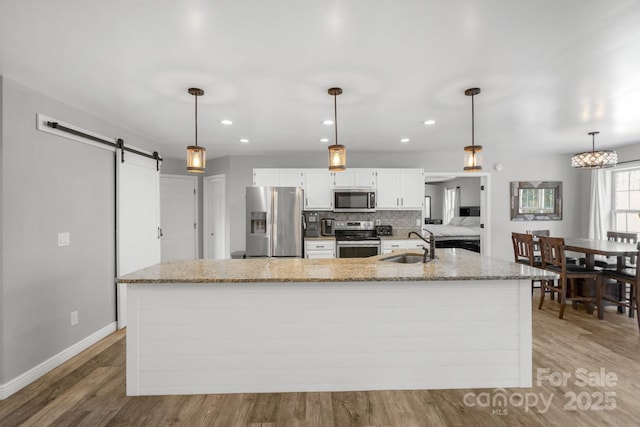 kitchen featuring pendant lighting, white cabinets, stainless steel appliances, sink, and a barn door