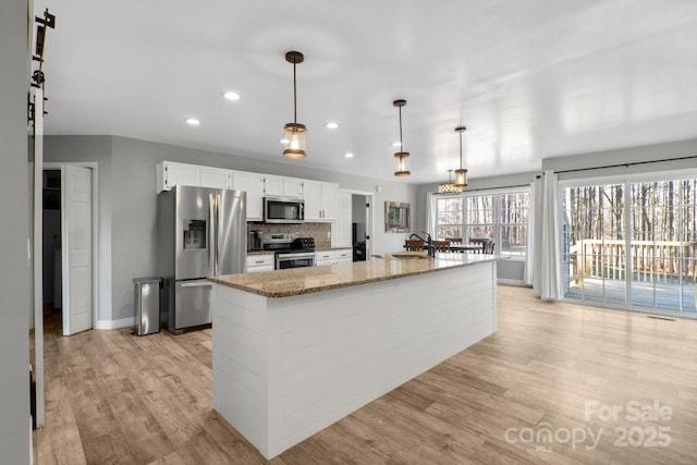 kitchen with light stone countertops, decorative light fixtures, white cabinetry, stainless steel appliances, and tasteful backsplash