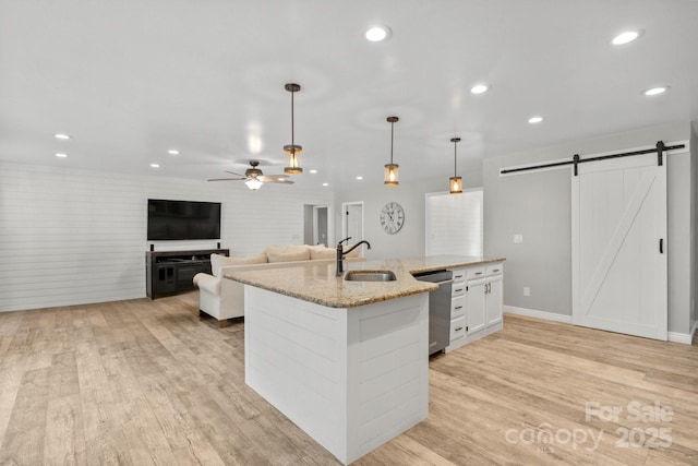 kitchen with decorative light fixtures, a barn door, dishwasher, white cabinets, and light stone counters