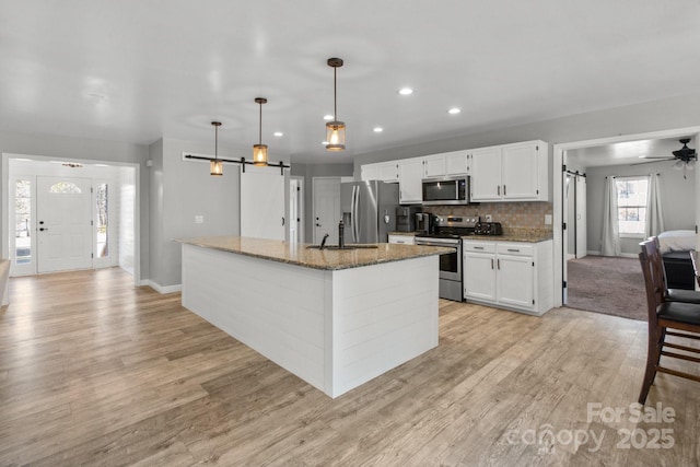 kitchen with white cabinetry, stainless steel appliances, an island with sink, dark stone countertops, and hanging light fixtures