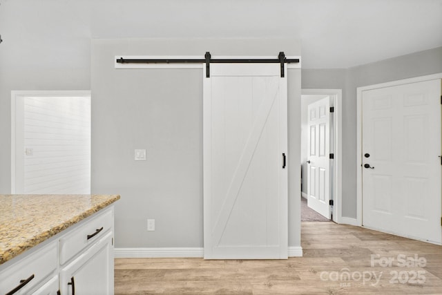 kitchen featuring white cabinetry, light hardwood / wood-style floors, a barn door, and light stone countertops