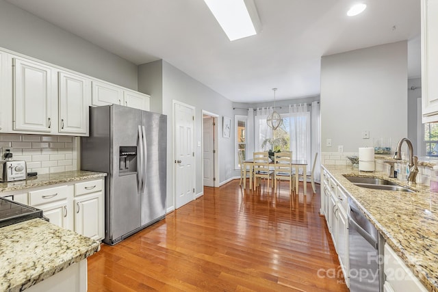 kitchen with pendant lighting, stainless steel appliances, decorative backsplash, white cabinetry, and sink