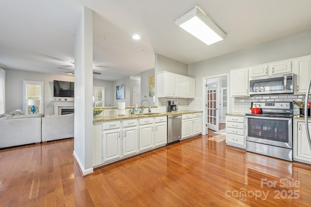 kitchen with stainless steel appliances, sink, white cabinetry, ceiling fan, and backsplash