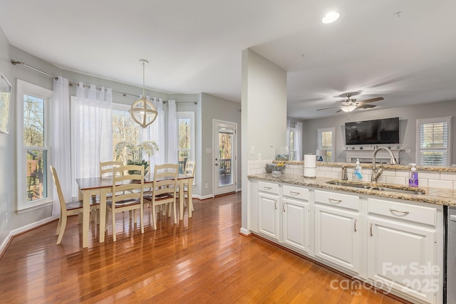 kitchen featuring pendant lighting, light wood-type flooring, ceiling fan with notable chandelier, white cabinets, and sink