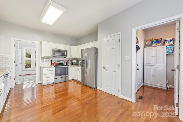 kitchen with white cabinets, stainless steel appliances, light hardwood / wood-style flooring, and tasteful backsplash