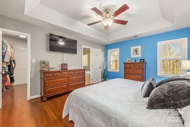 bedroom with ceiling fan, ensuite bath, a raised ceiling, and dark hardwood / wood-style floors