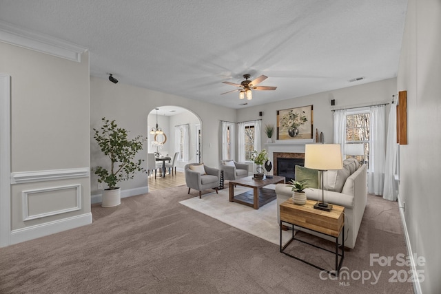 living room with ceiling fan, a premium fireplace, light carpet, and a textured ceiling