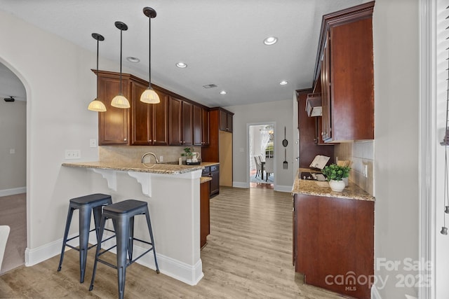 kitchen with light stone counters, decorative light fixtures, light hardwood / wood-style floors, and decorative backsplash