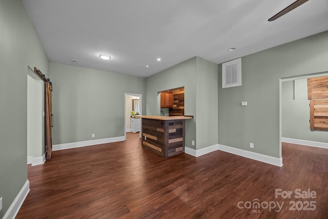 unfurnished living room featuring ceiling fan, a barn door, and dark hardwood / wood-style flooring