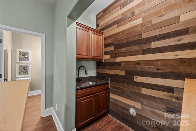 bar with sink, dark stone countertops, dark hardwood / wood-style floors, and wood walls