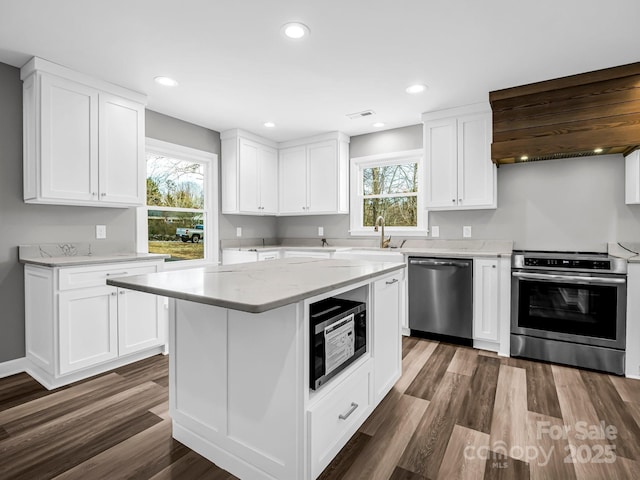 kitchen featuring appliances with stainless steel finishes, white cabinets, a kitchen island, dark wood-type flooring, and plenty of natural light