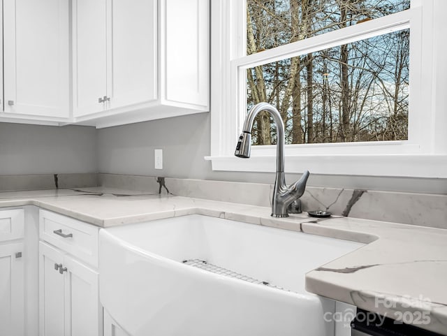 interior details with light stone counters, sink, and white cabinetry