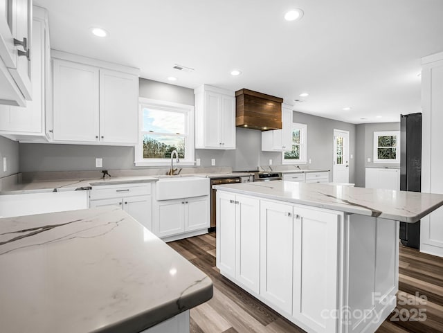 kitchen featuring custom range hood, sink, white cabinets, light stone counters, and a center island