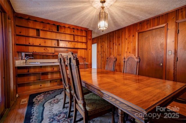 dining room with a textured ceiling, dark wood-type flooring, wooden walls, and sink