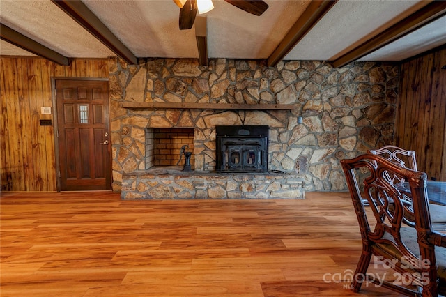 unfurnished living room with hardwood / wood-style flooring, a textured ceiling, wood walls, beam ceiling, and ceiling fan