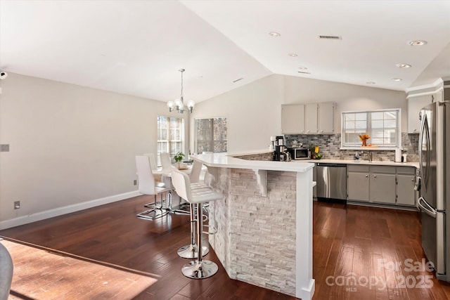 kitchen with dark wood-type flooring, backsplash, lofted ceiling, and stainless steel appliances