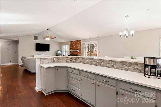 kitchen featuring lofted ceiling, a brick fireplace, gray cabinets, dark wood-type flooring, and ceiling fan with notable chandelier