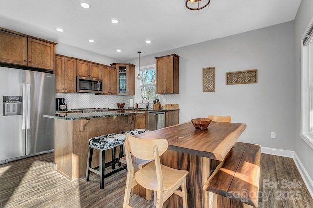 kitchen with appliances with stainless steel finishes, backsplash, dark hardwood / wood-style floors, dark stone countertops, and hanging light fixtures