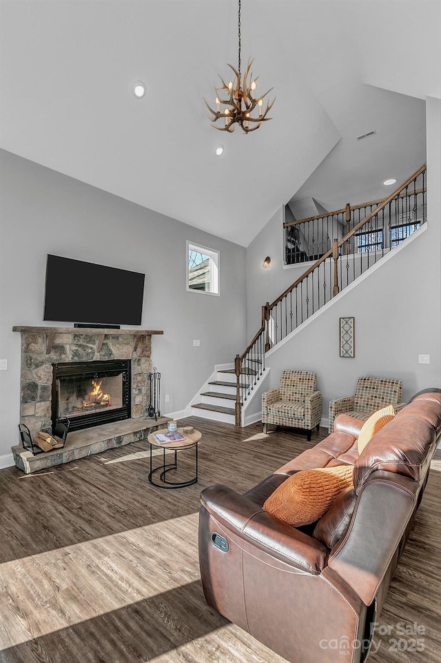 living room with high vaulted ceiling, dark hardwood / wood-style flooring, a stone fireplace, and an inviting chandelier