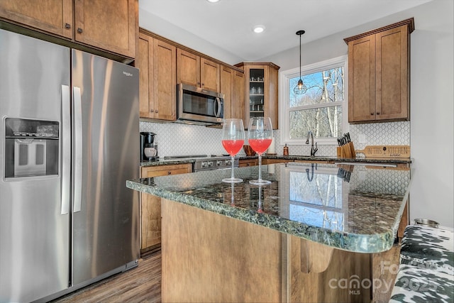 kitchen featuring light hardwood / wood-style floors, stainless steel appliances, backsplash, dark stone countertops, and pendant lighting