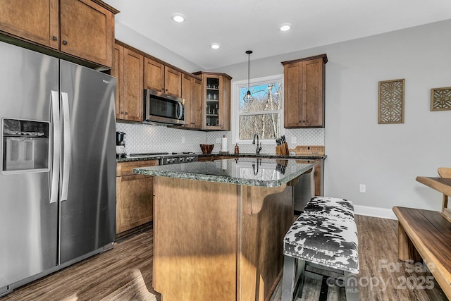 kitchen featuring pendant lighting, dark hardwood / wood-style flooring, appliances with stainless steel finishes, a breakfast bar area, and dark stone counters