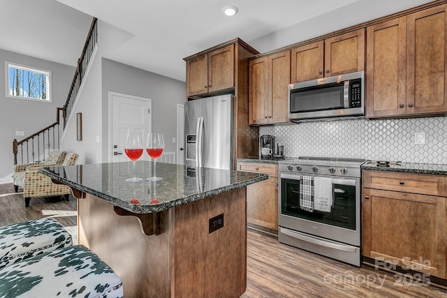 kitchen with hardwood / wood-style floors, appliances with stainless steel finishes, a kitchen bar, tasteful backsplash, and dark stone countertops