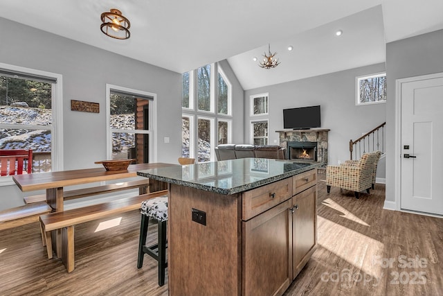 kitchen featuring light wood-type flooring, dark stone countertops, a fireplace, a chandelier, and a center island