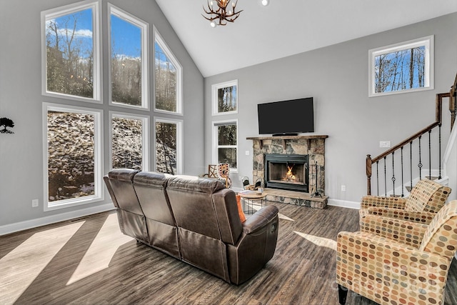 living room with an inviting chandelier, hardwood / wood-style floors, a stone fireplace, and high vaulted ceiling