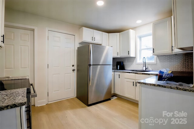 kitchen featuring white cabinets, tasteful backsplash, sink, stainless steel refrigerator, and light wood-type flooring