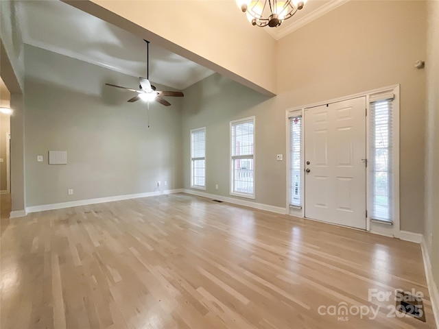 entrance foyer with ceiling fan with notable chandelier, ornamental molding, light hardwood / wood-style floors, and a towering ceiling