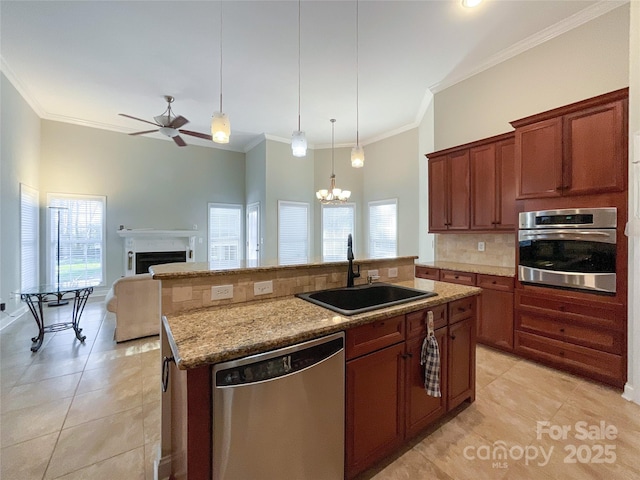 kitchen featuring ceiling fan with notable chandelier, stainless steel appliances, an island with sink, sink, and hanging light fixtures