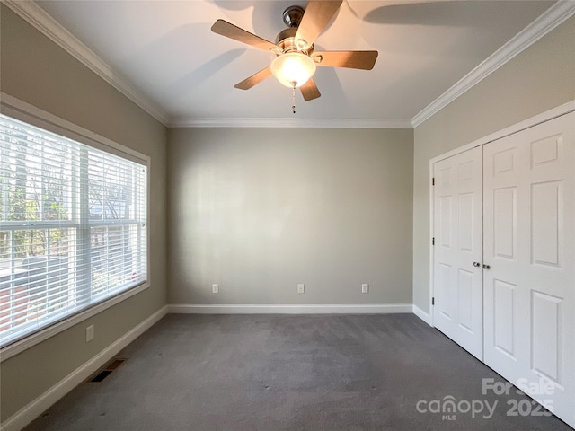 unfurnished bedroom with ceiling fan, a closet, dark carpet, and ornamental molding