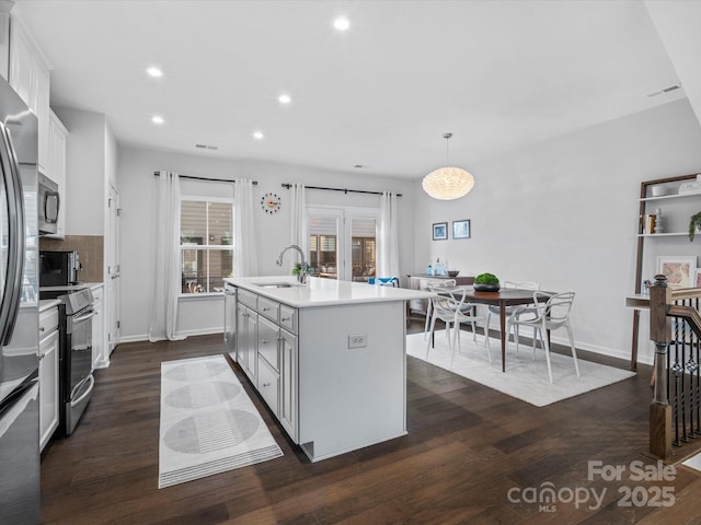 kitchen featuring sink, hanging light fixtures, a kitchen island with sink, stainless steel appliances, and white cabinets