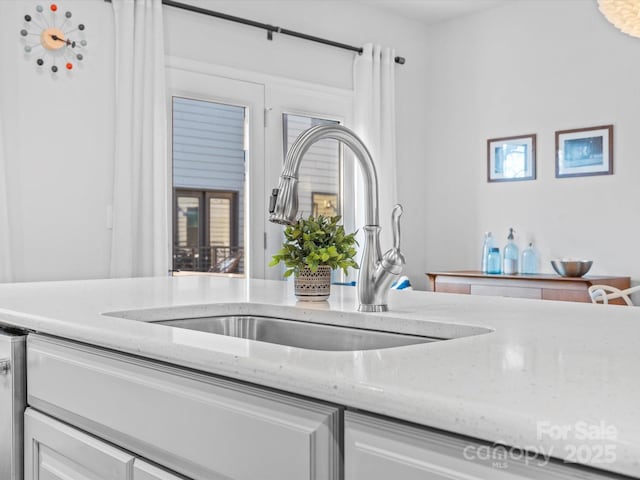 kitchen with white cabinets, light stone counters, and sink