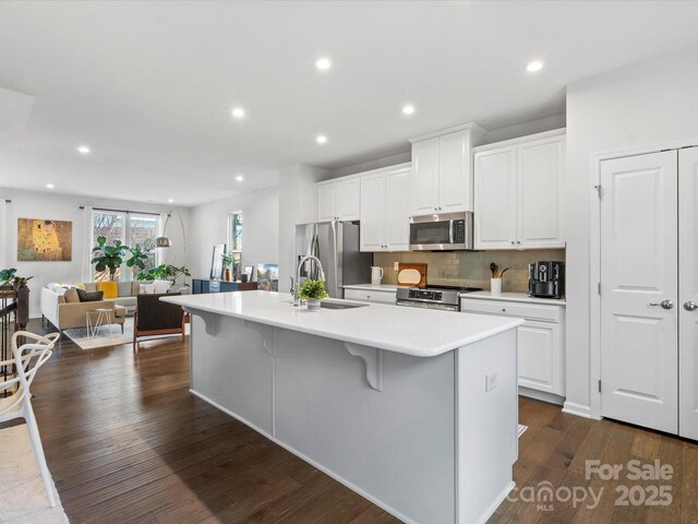 kitchen with white cabinets, a kitchen bar, stainless steel appliances, dark hardwood / wood-style floors, and a center island with sink