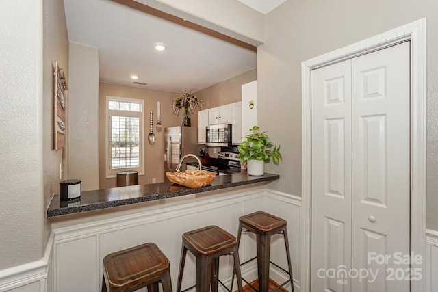 kitchen with white cabinetry, kitchen peninsula, stainless steel appliances, a kitchen breakfast bar, and sink