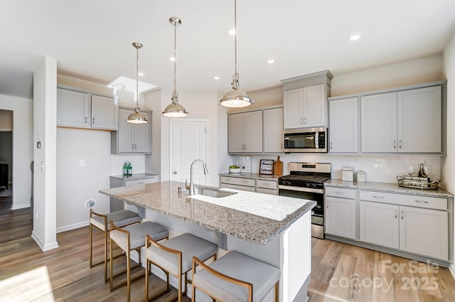 kitchen featuring sink, a center island with sink, pendant lighting, gray cabinetry, and appliances with stainless steel finishes