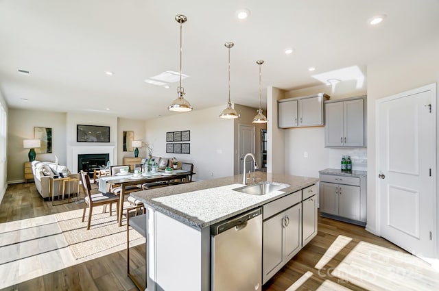 kitchen featuring stainless steel dishwasher, a center island with sink, gray cabinetry, and sink