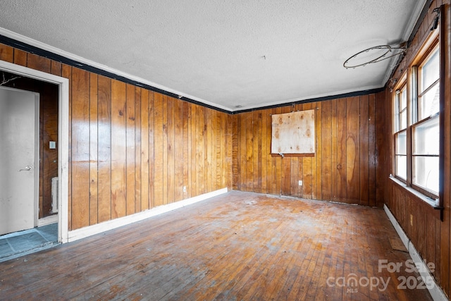 unfurnished room featuring wood walls, ornamental molding, and wood-type flooring