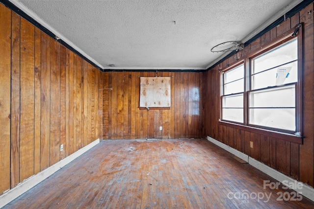 empty room with a textured ceiling, wooden walls, dark hardwood / wood-style floors, and ornamental molding