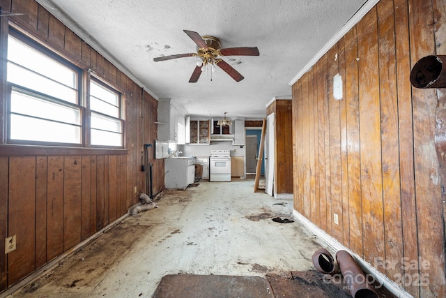 unfurnished living room featuring ceiling fan, wood walls, crown molding, and a textured ceiling