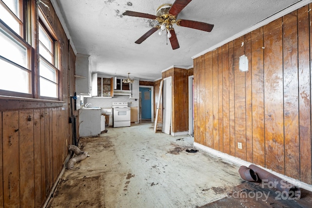 unfurnished living room featuring ornamental molding, ceiling fan with notable chandelier, wooden walls, and a textured ceiling