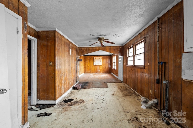 interior space with a textured ceiling, ornamental molding, and wooden walls