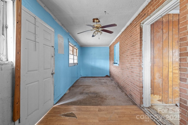 corridor with brick wall, crown molding, a textured ceiling, and light wood-type flooring